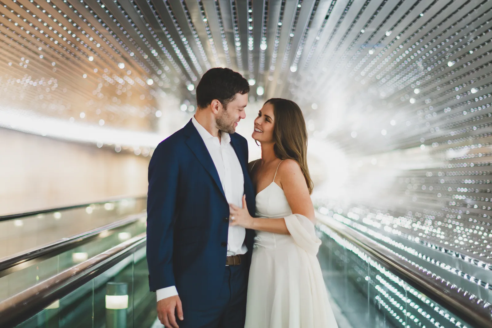 Smiling together on the moving walkway under a ceiling of lights
