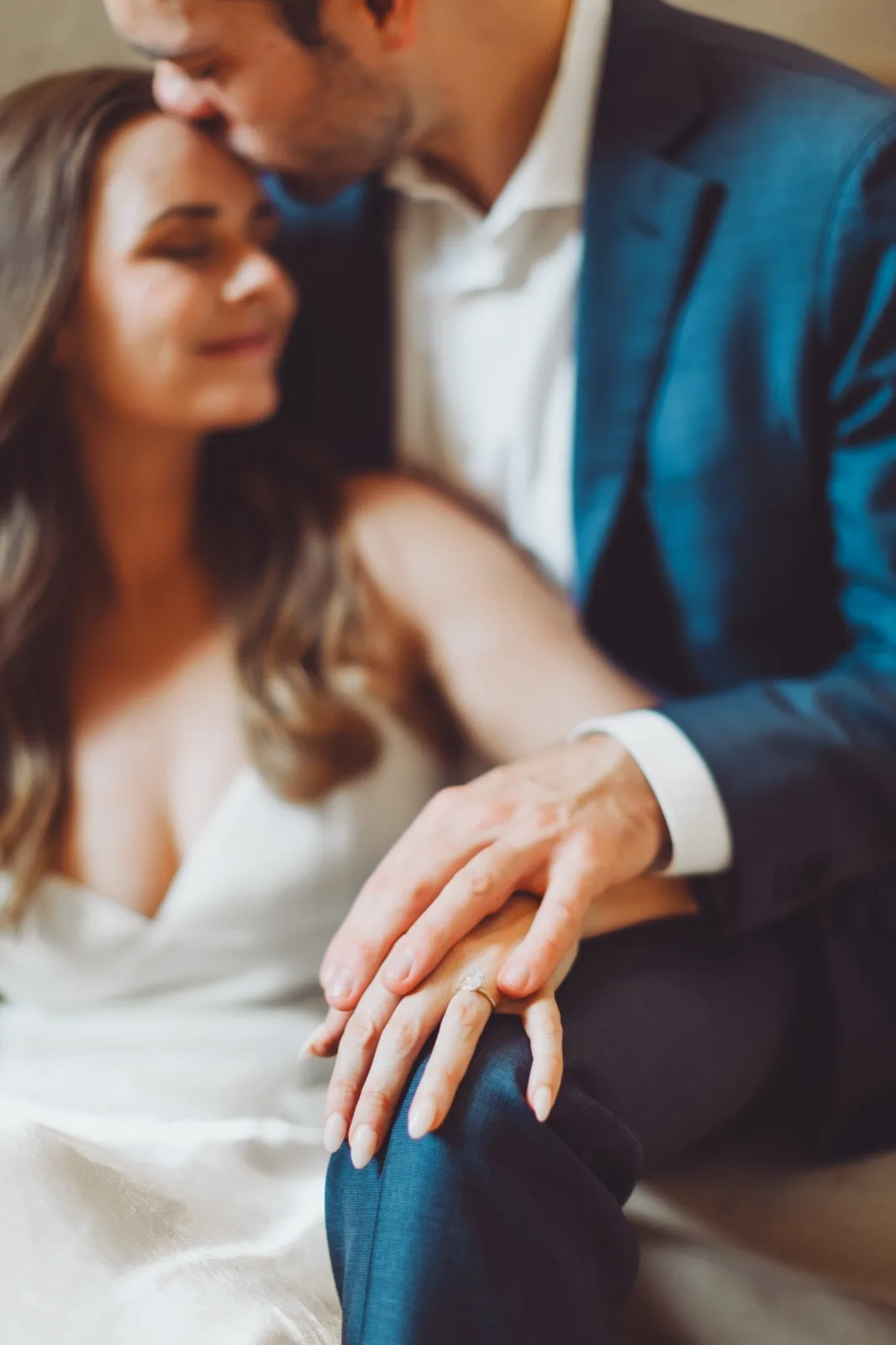 A kiss on her forehead, the ring resting in focus on his knee